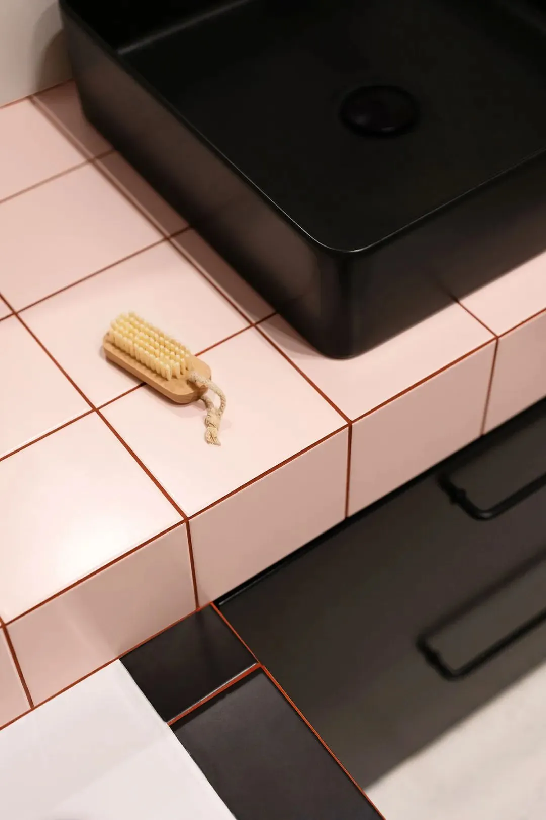 A minimalist bathroom with a black sink and pink ceramic tiles.