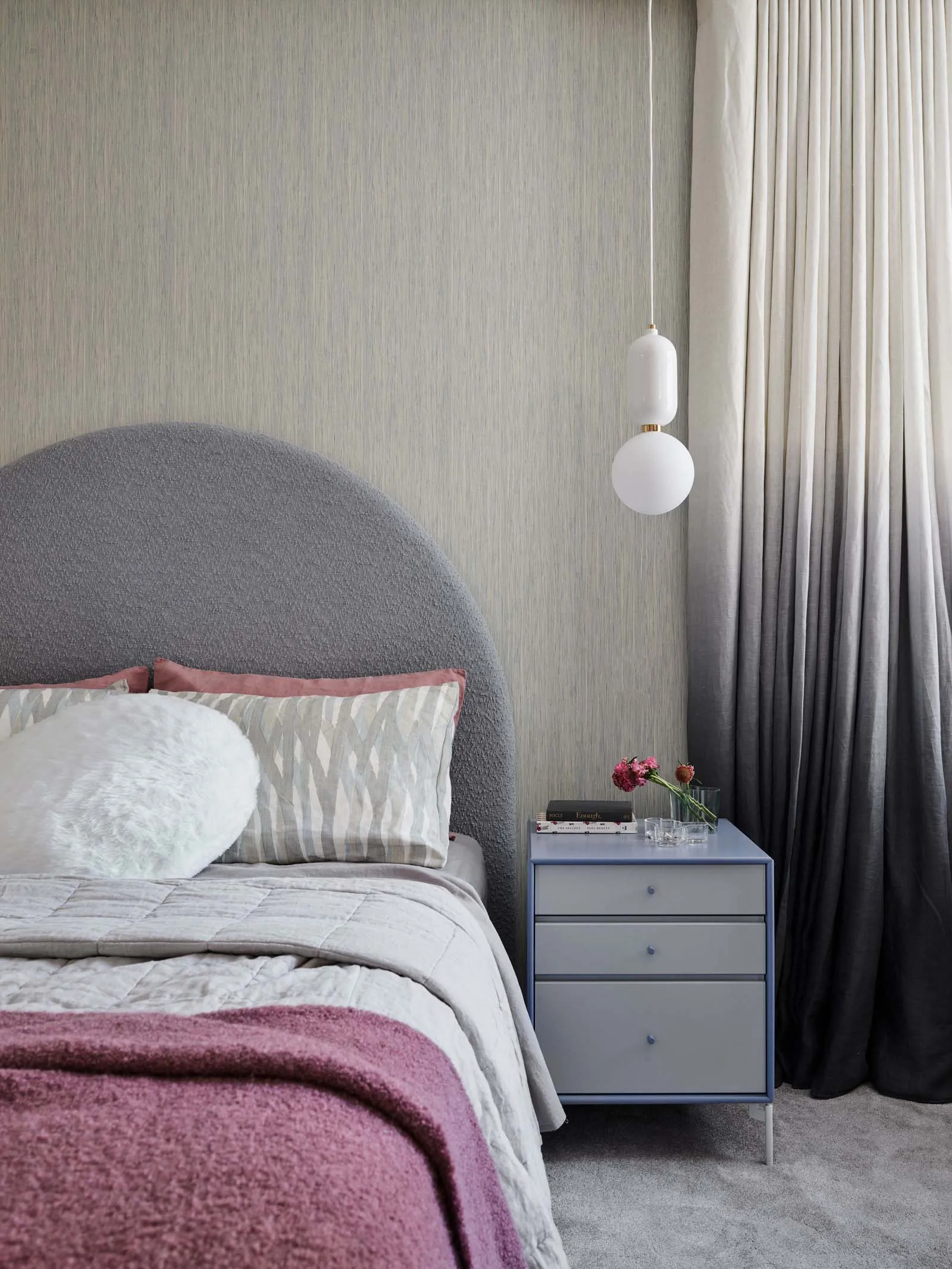 Bedroom with grey textured fabric headboard, grey walls, and wooden nightstand.