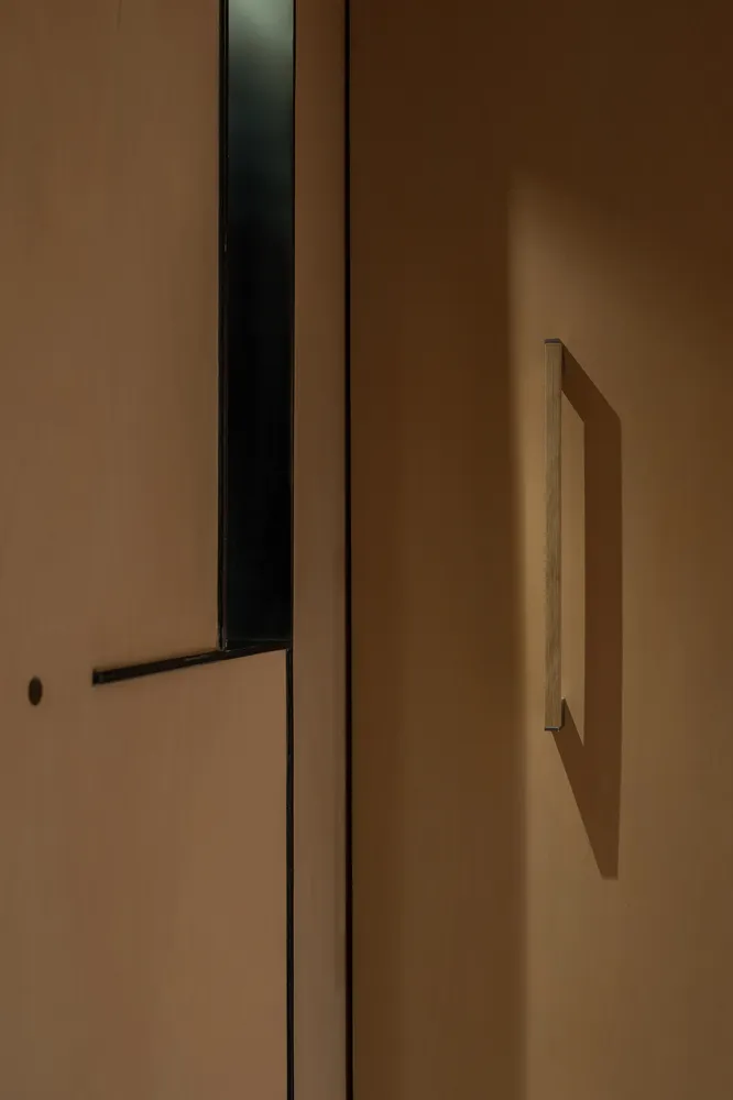 A contemporary steel door handle mounted on a brown wooden surface with a rectangular cutout detail.