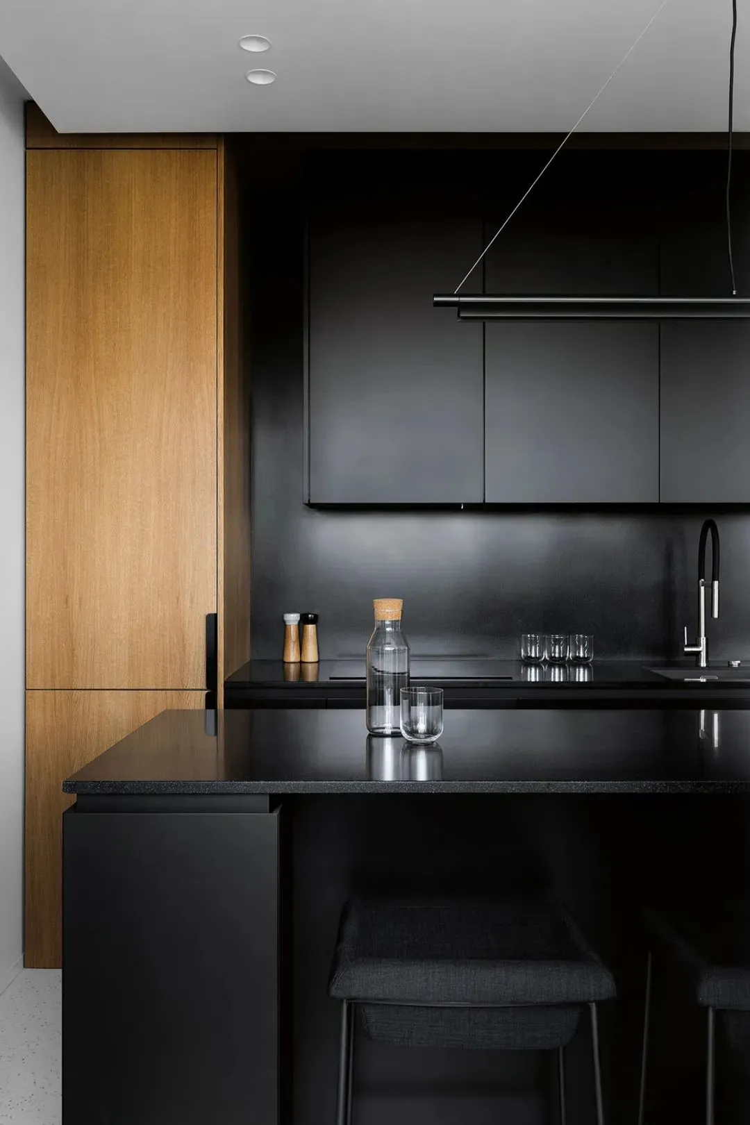 A modern black kitchen with wooden cabinets, black countertops, and minimalist design.