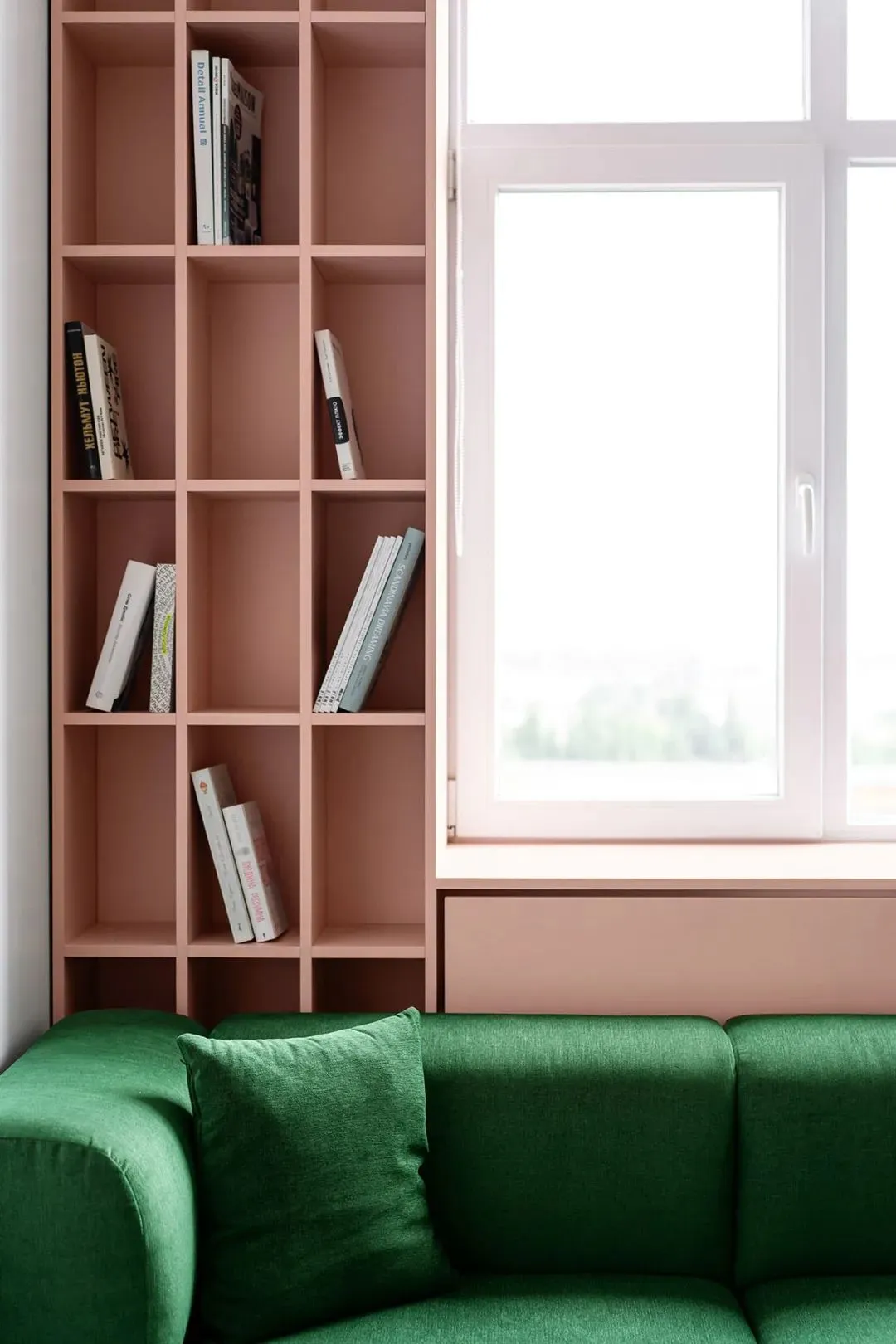 A modern living room featuring a green sofa with a bookshelf and a window.