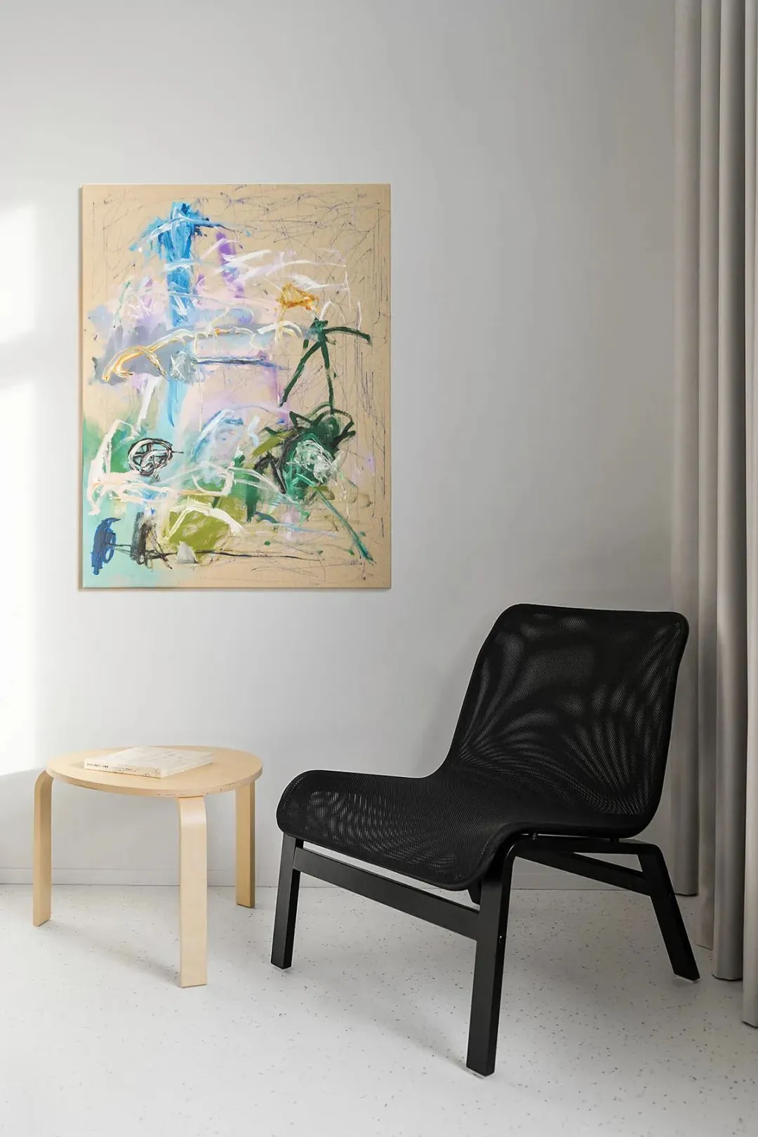 A modern black frame chair in a minimalist living room setting with an abstract painting on the wall and a round wooden side