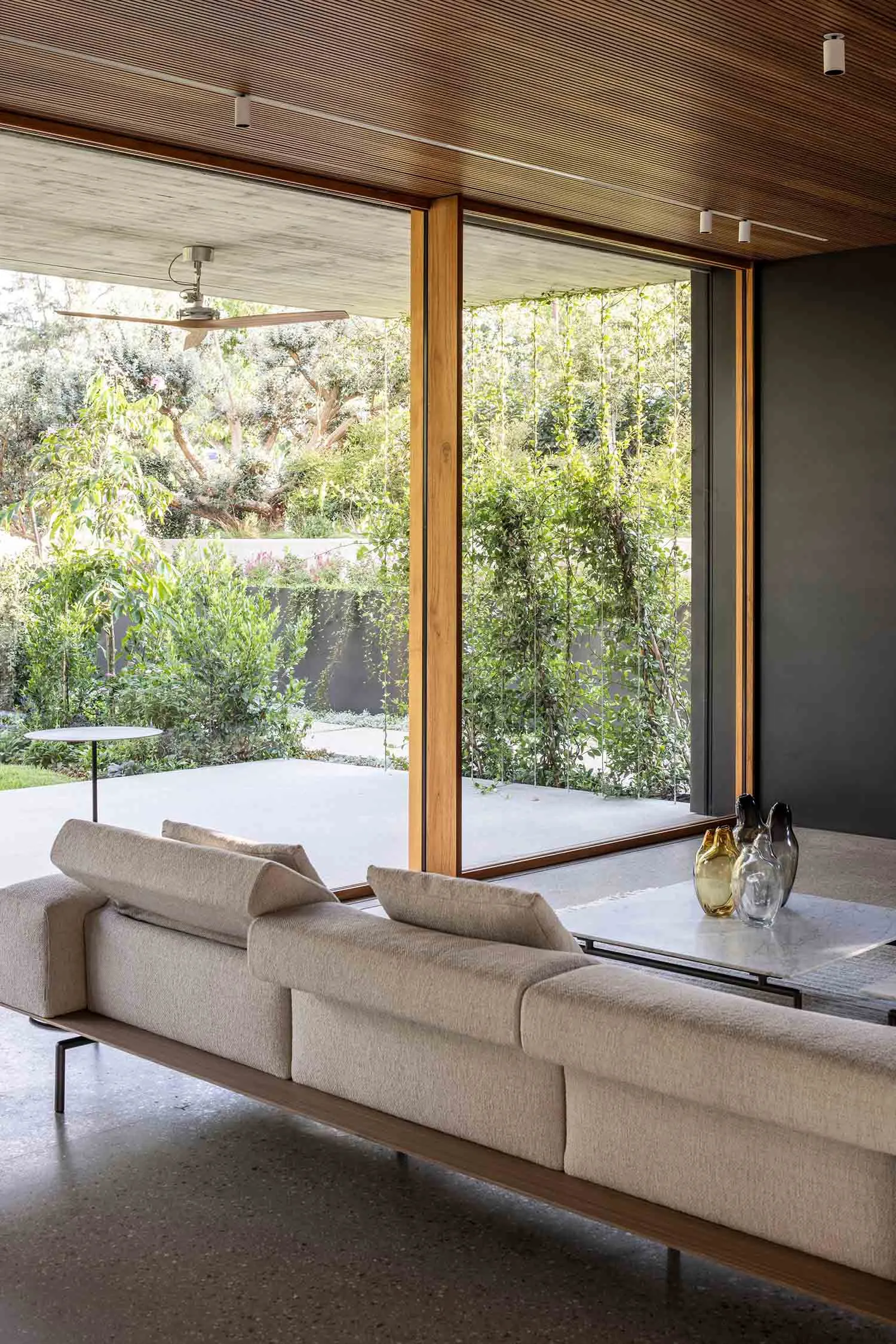 A modern living room featuring a wooden ceiling and large windows overlooking greenery.
