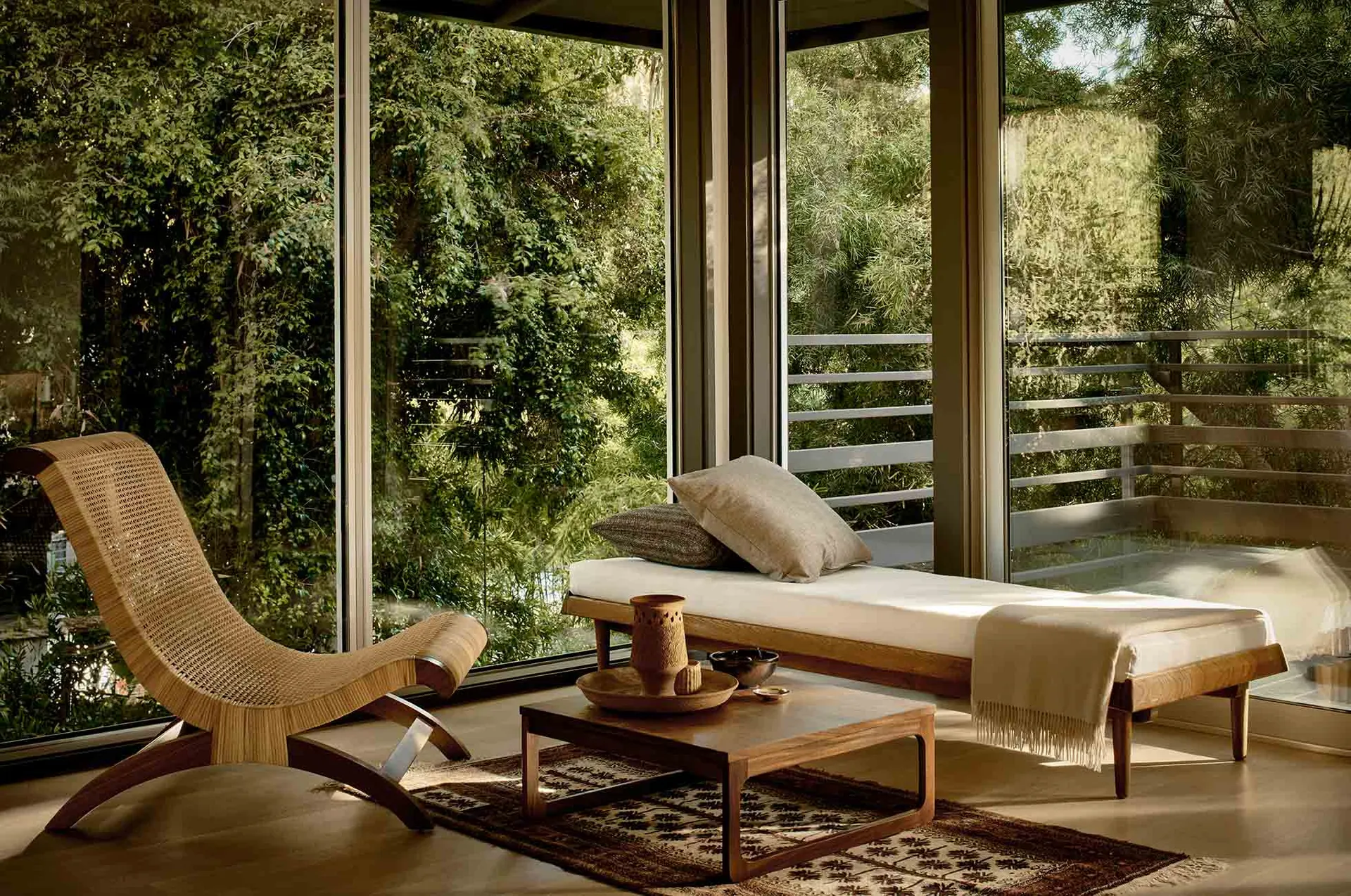 A minimalist living room with wooden furniture, fabric cushions, and glass walls.