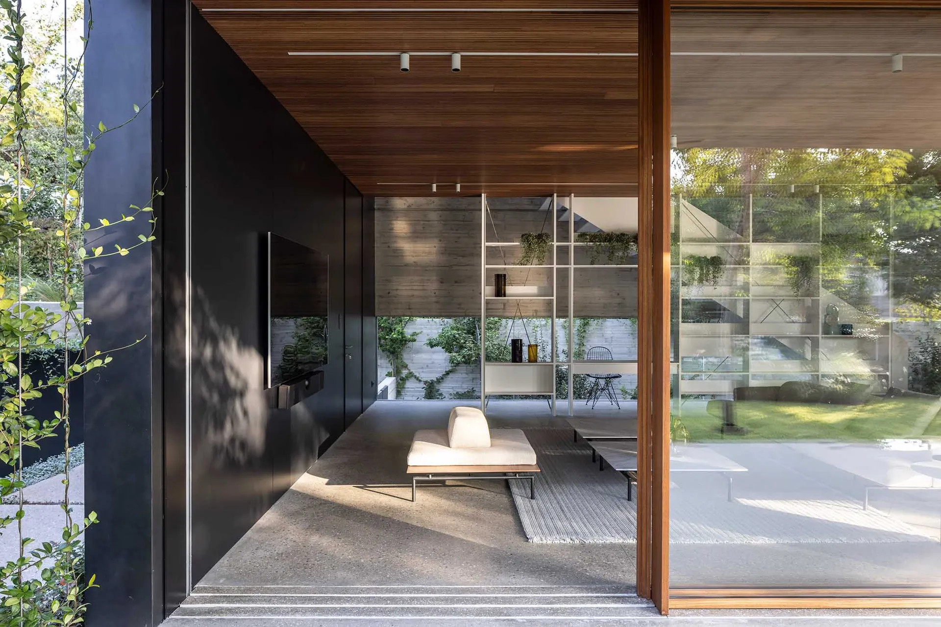 Modern living room with minimalist furniture and glass walls providing a connection to the outdoor green space.