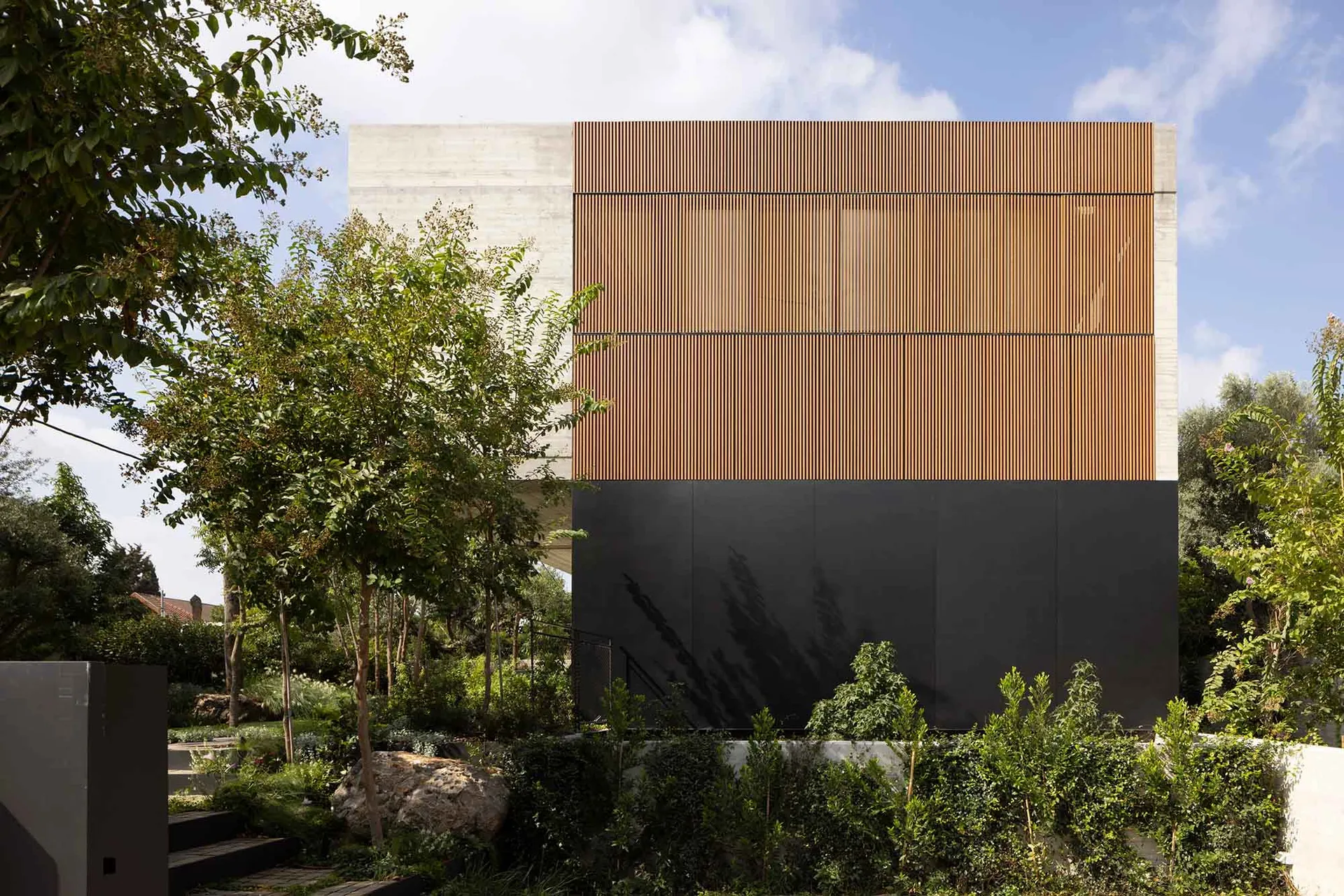 A modern house with a wooden facade and concrete lower sections surrounded by lush greenery.