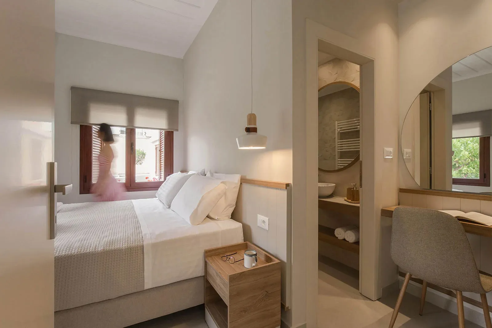 A minimalist bedroom with a white and neutral color theme, featuring a bed, nightstand, and bathroom access