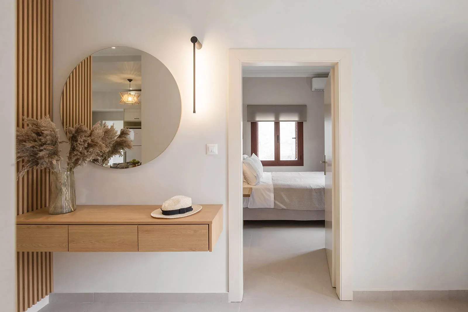 A minimalist bedroom featuring a wooden desk and white walls, with a view into the adjoining room.