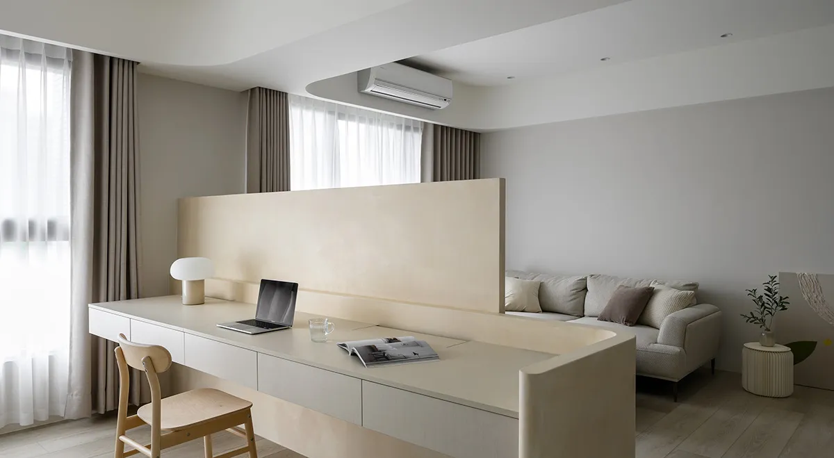 A minimalist living room with neutral tones, featuring a integrated desk and seating area