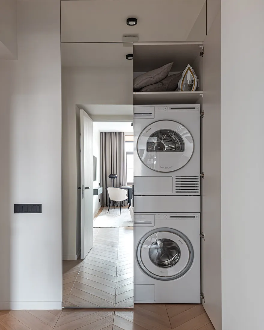 Modern minimalist laundry room featuring sleek metal appliances and glass panels, with a wooden herringbone floor.