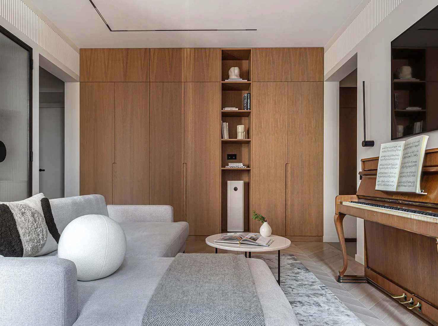 Minimalist living room featuring a grey sofa, a round white ball ottoman, a wooden cabinet, a piano with sheet music, and a r