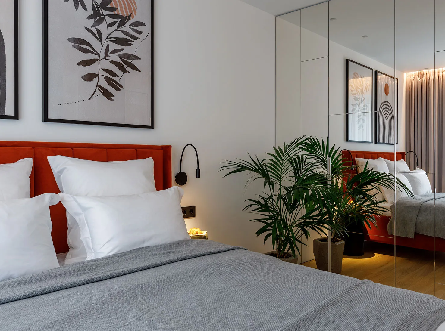 A minimalist bedroom with a textured fabric headboard, potted palm plant, and modern abstract artwork.
