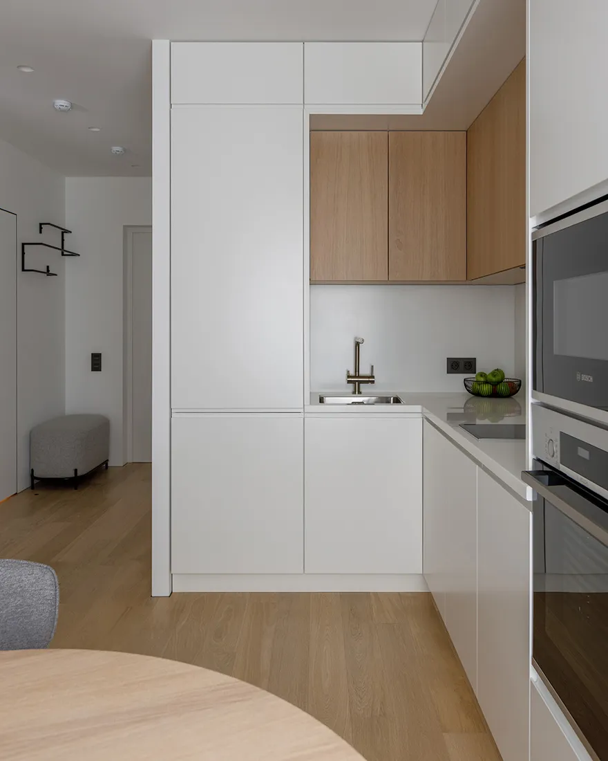 Modern, minimalist residential kitchen with white laminate cabinets and wood flooring.