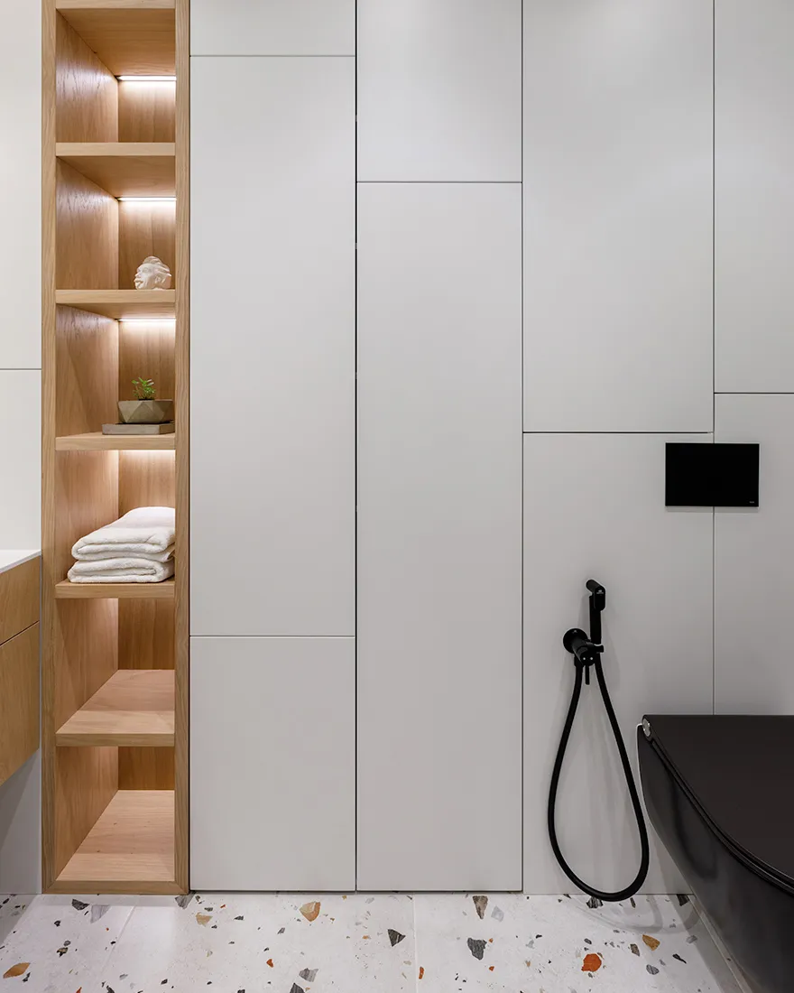 Modern minimalist bathroom with wood shelves, white cabinets, and terrazzo floor tiles.
