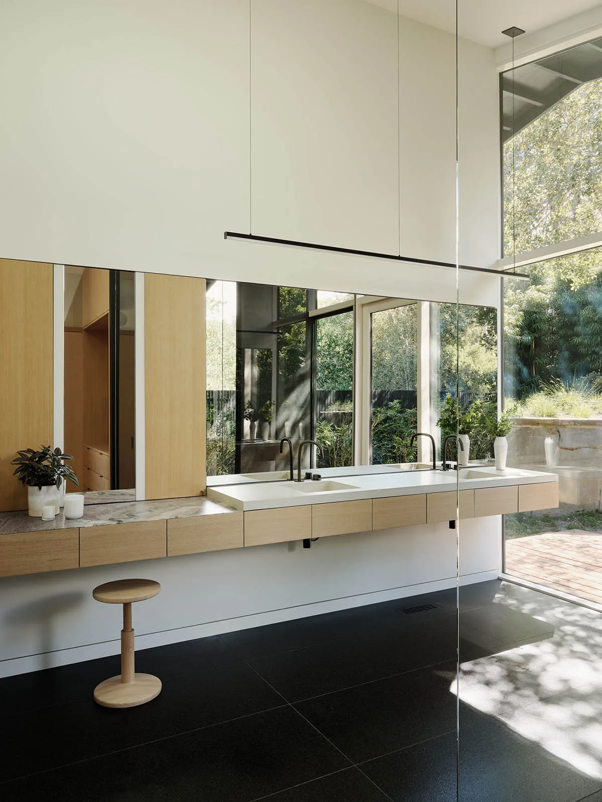 A modern bathroom featuring a floating vanity with dark wood cabinets, glass shower enclosure, and large windows overlooking