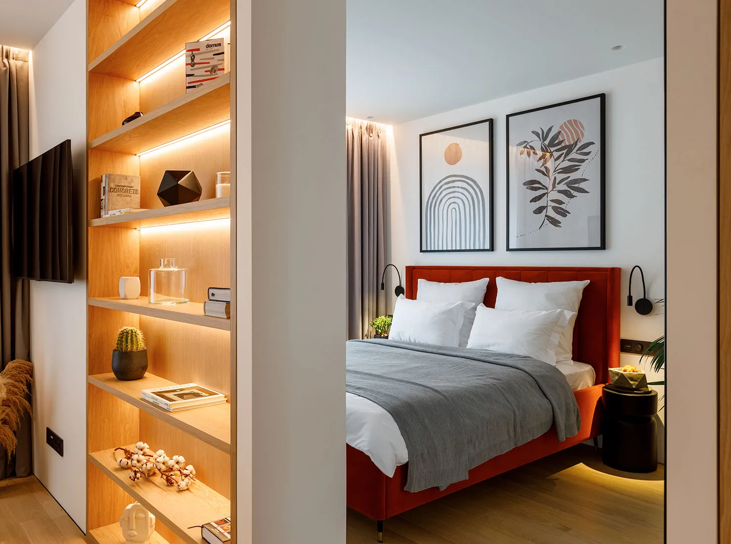 A cozy modern bedroom featuring a red upholstered bed with white pillows and a gray blanket, illuminated by warm under-shelf