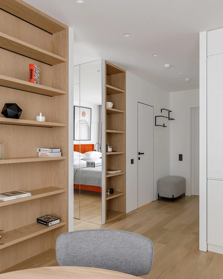 A modern interior design featuring wooden shelves with books and decor items, leading to a bedroom with a comfortable bed.