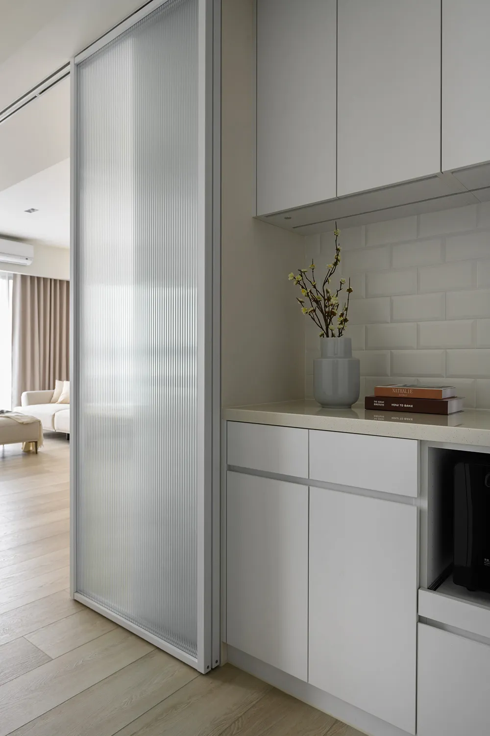 A modern kitchen featuring a glass panel wall with a white cabinet and countertop, and a vase with flowers.