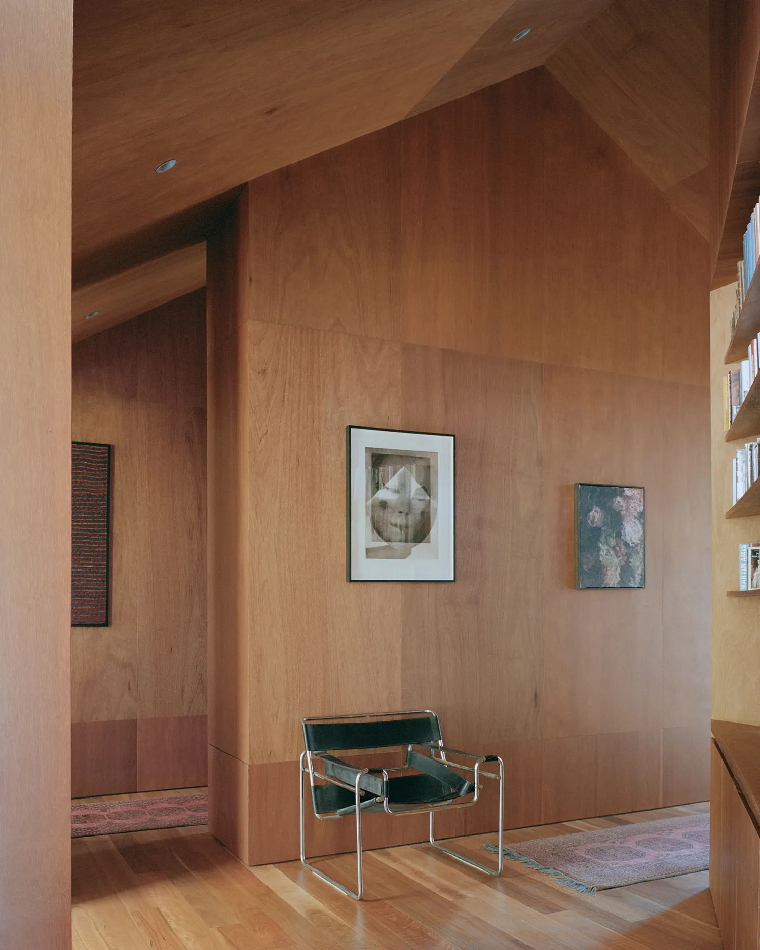 A minimalist living room with wood paneling, featuring a modern chair and framed artwork.