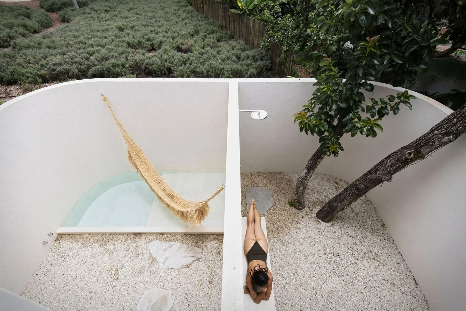 A minimalist outdoor patio featuring concrete walls, sand flooring, and a natural fiber hammock.