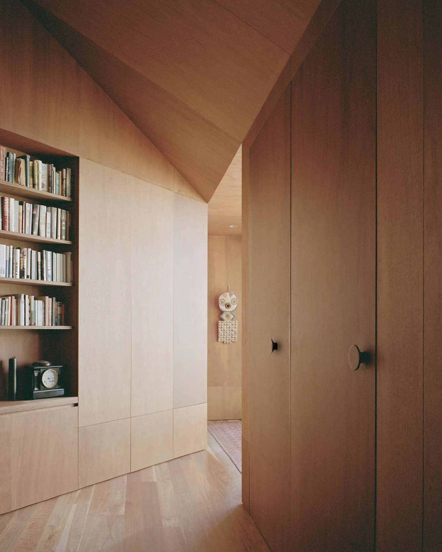 A modern minimalist residential closet featuring wooden shelves and doors.