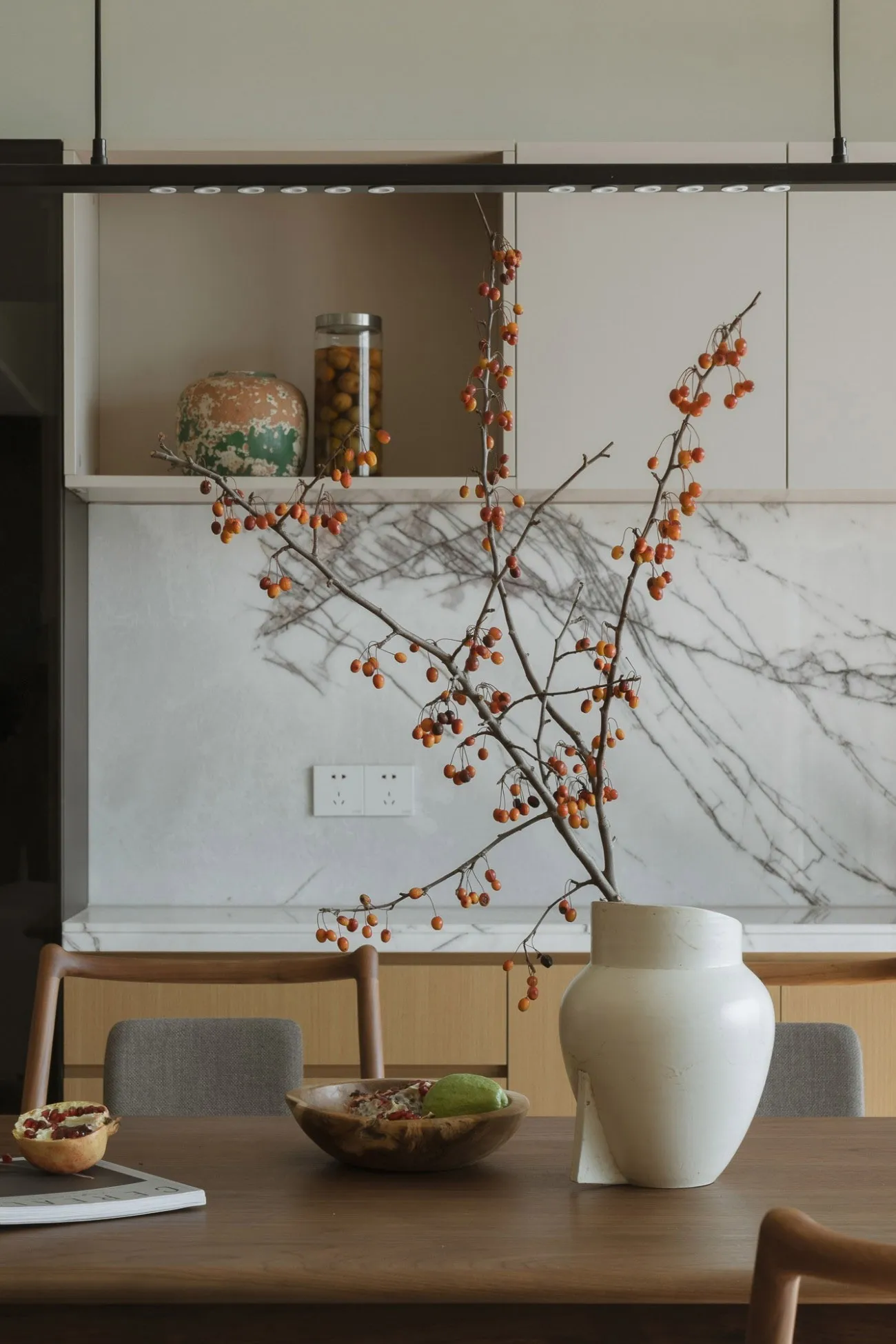 A modern kitchen with wooden elements and a vase with berries on a table.