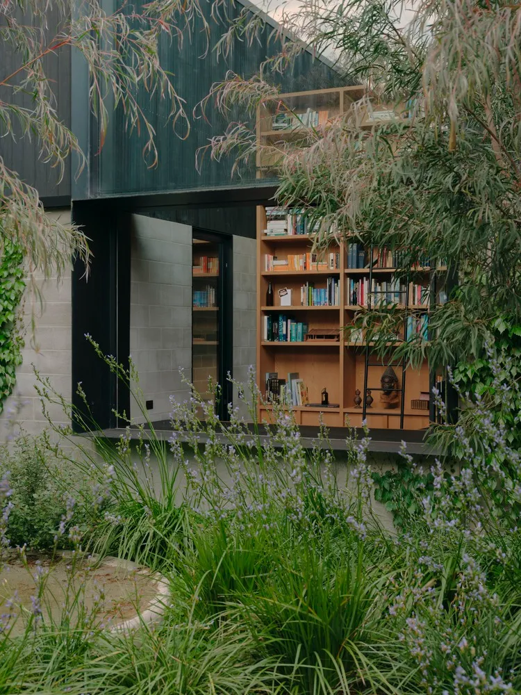 A modern residential garden featuring a wooden bookshelf with a variety of books.
