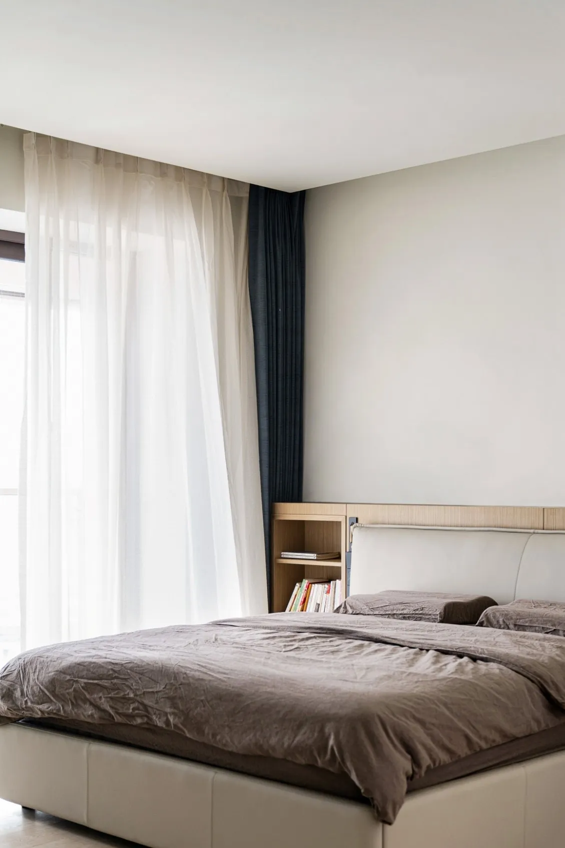 Minimalist bedroom featuring a large bed with white curtains and wooden walls.