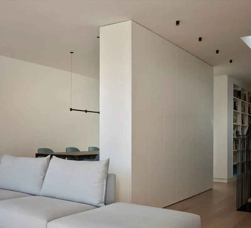 A minimalist living room with light-colored wood flooring, white couch, and unadorned walls.