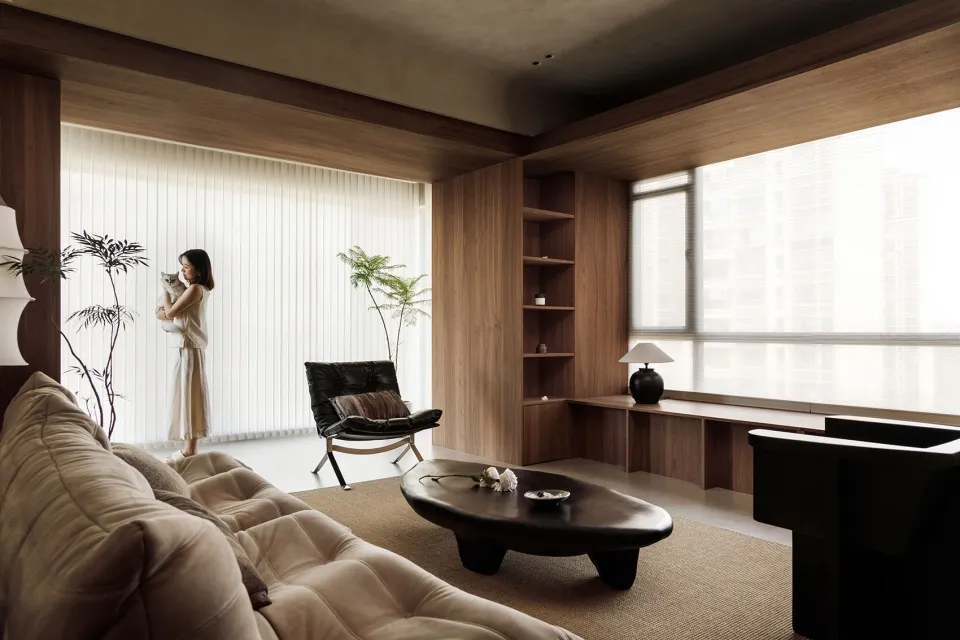 A minimalist living room with a large brown couch, black coffee table, and wooden shelves.