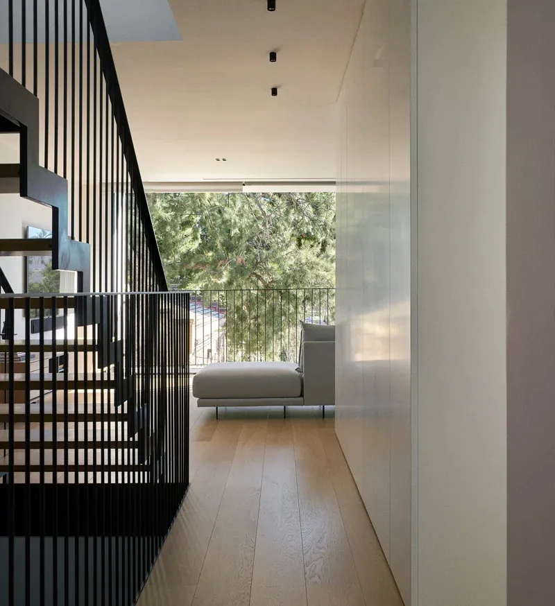 A minimalist modern residential interior with wooden flooring and a large window overlooking greenery.