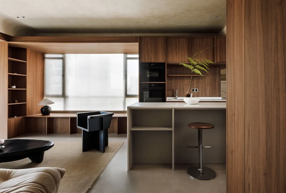 A modern residential kitchen featuring walnut furniture, black stools, and a minimalist design.