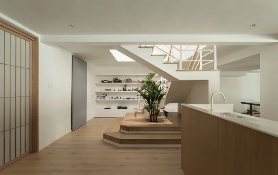 Modern interior design featuring a living room with a kitchen area and a staircase, using wood and white materials.