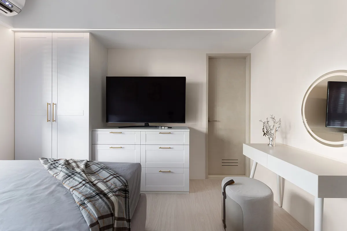 A modern bedroom with white furniture and a television on a cabinet.