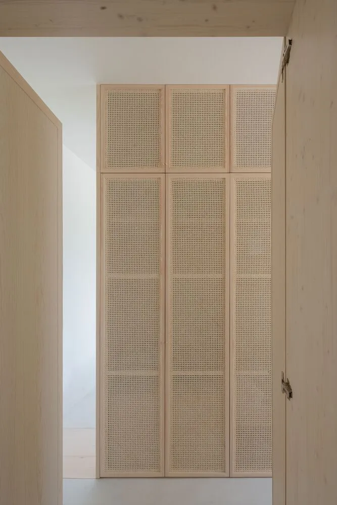 A tall, wooden closet with cane mesh doors and a light, open design.
