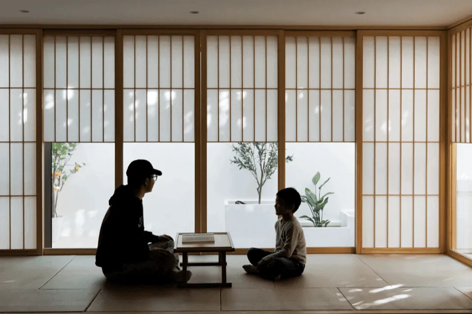 Two people in silhouette sitting in a room with wooden sliding doors and a plant in the background.