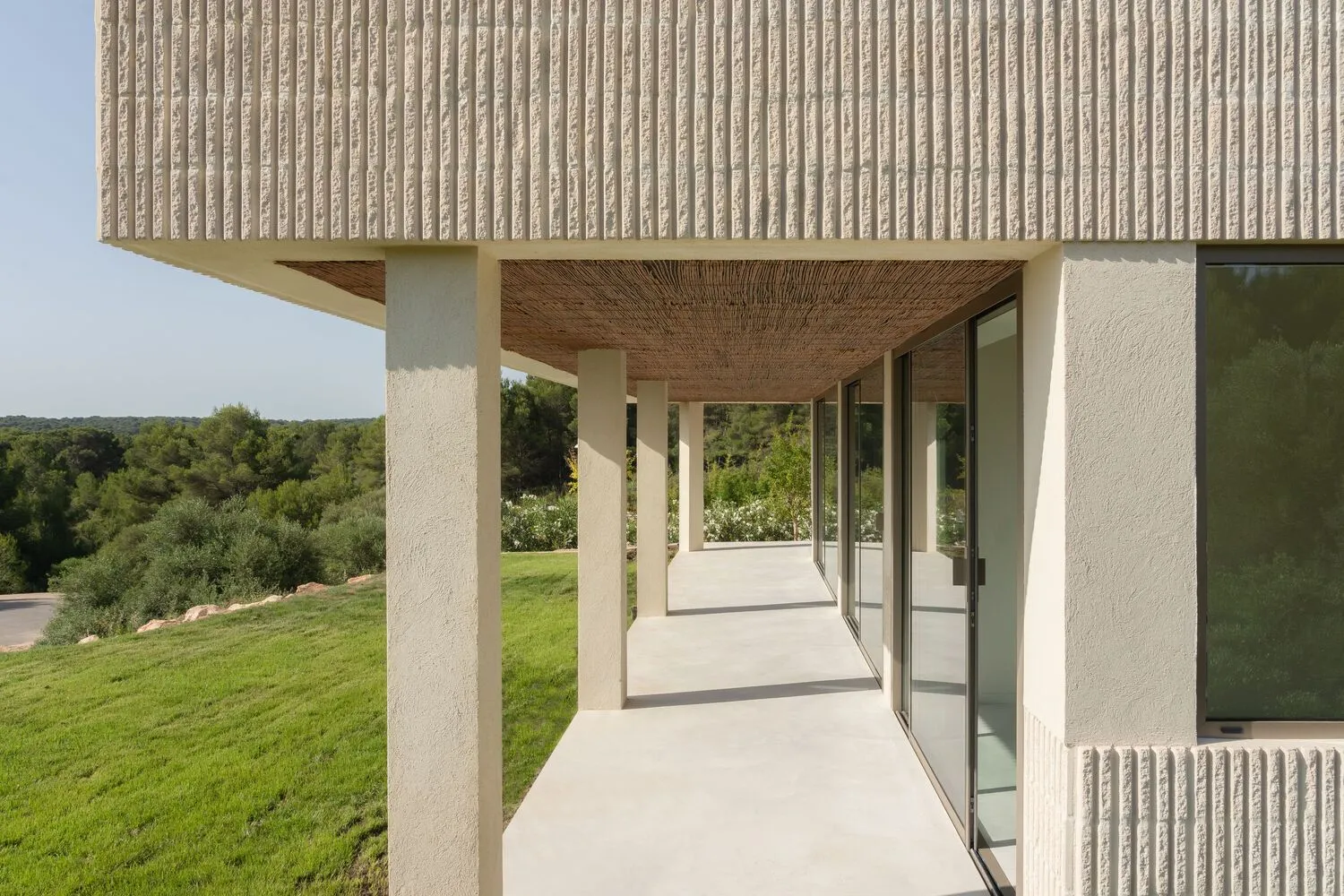 Modern residential building with concrete exterior and large glass windows overlooking green landscape.