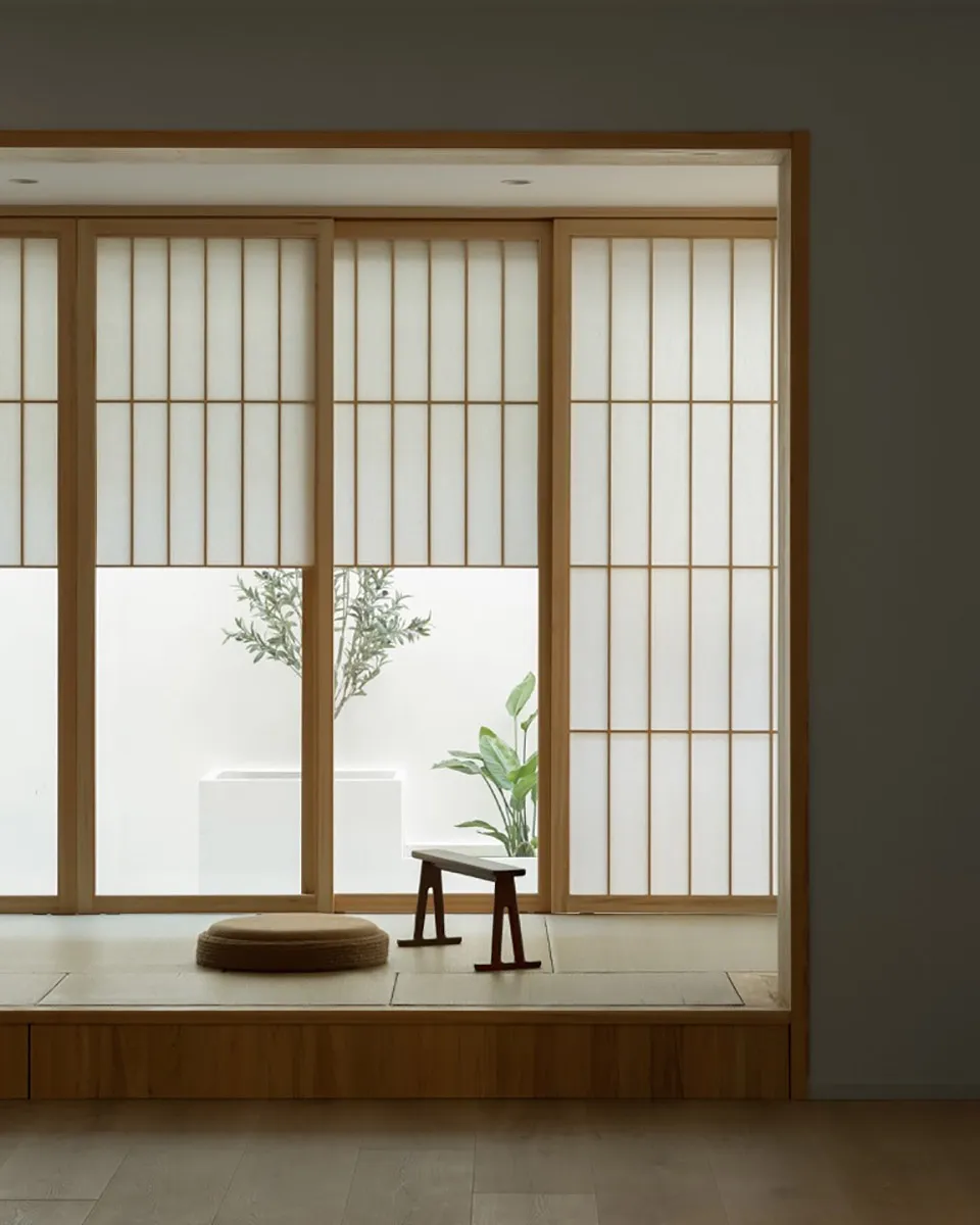 A minimalist living space featuring wooden flooring, paper screens with wooden frames, and a low wooden stool with a cushion.