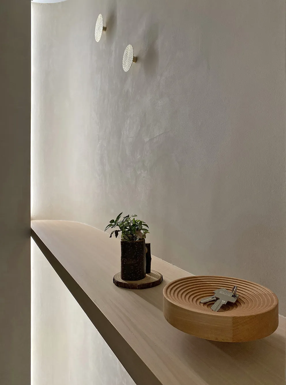 A minimalist wall shelf with a wooden bowl holding keys and a small plant pot.