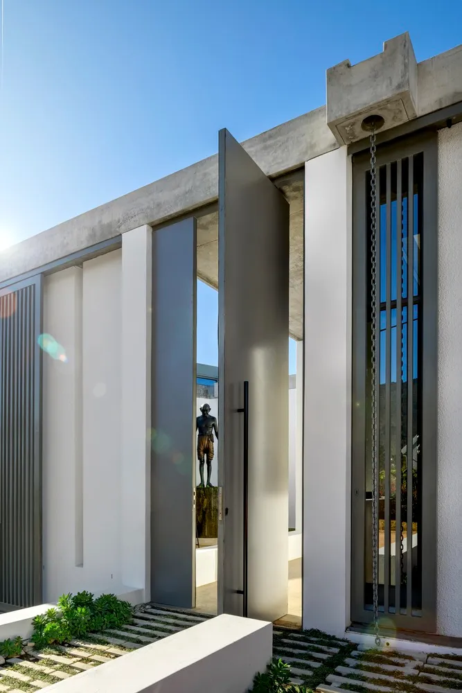 Modern exterior architectural design featuring a concrete and glass entryway bordered by a botanical garden.