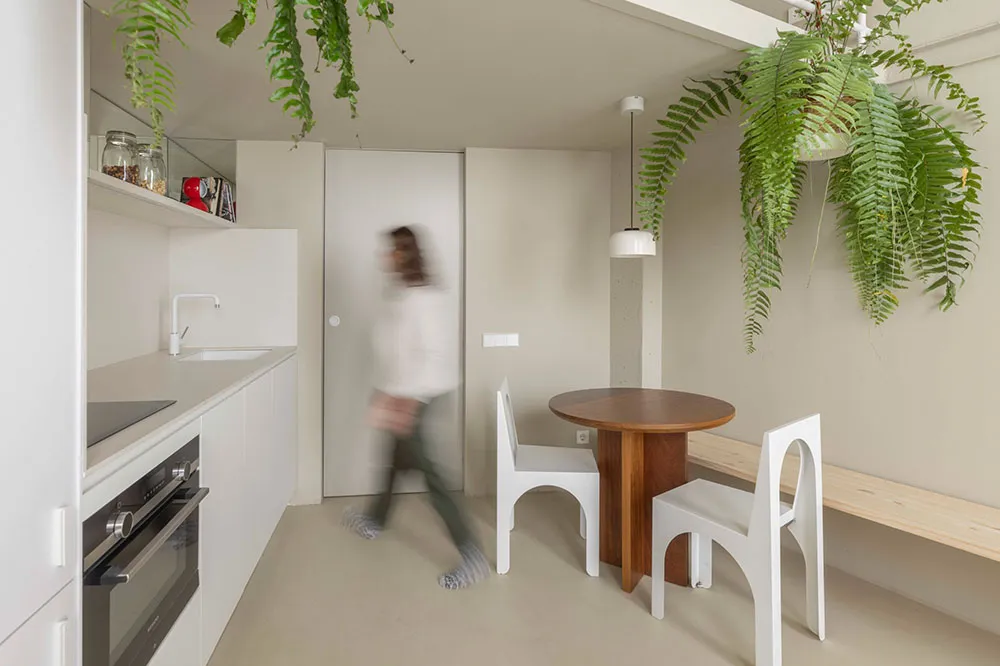 A modern kitchen with white minimalist design, featuring a wooden table, white chairs, and glass materials.