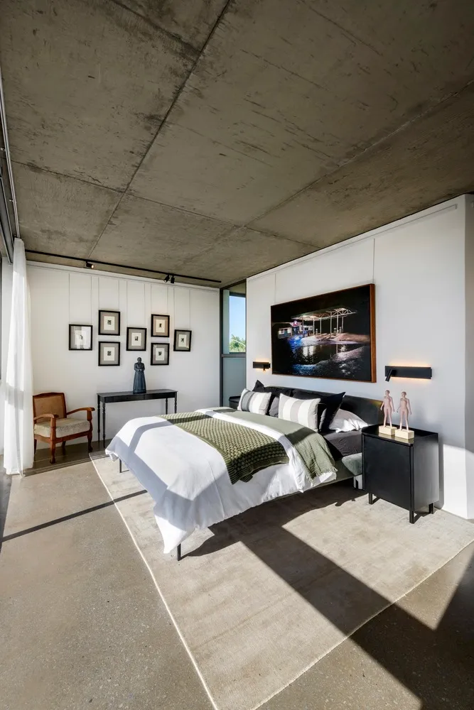 A modern industrial bedroom with concrete walls, a bed, and various framed pictures on the wall.