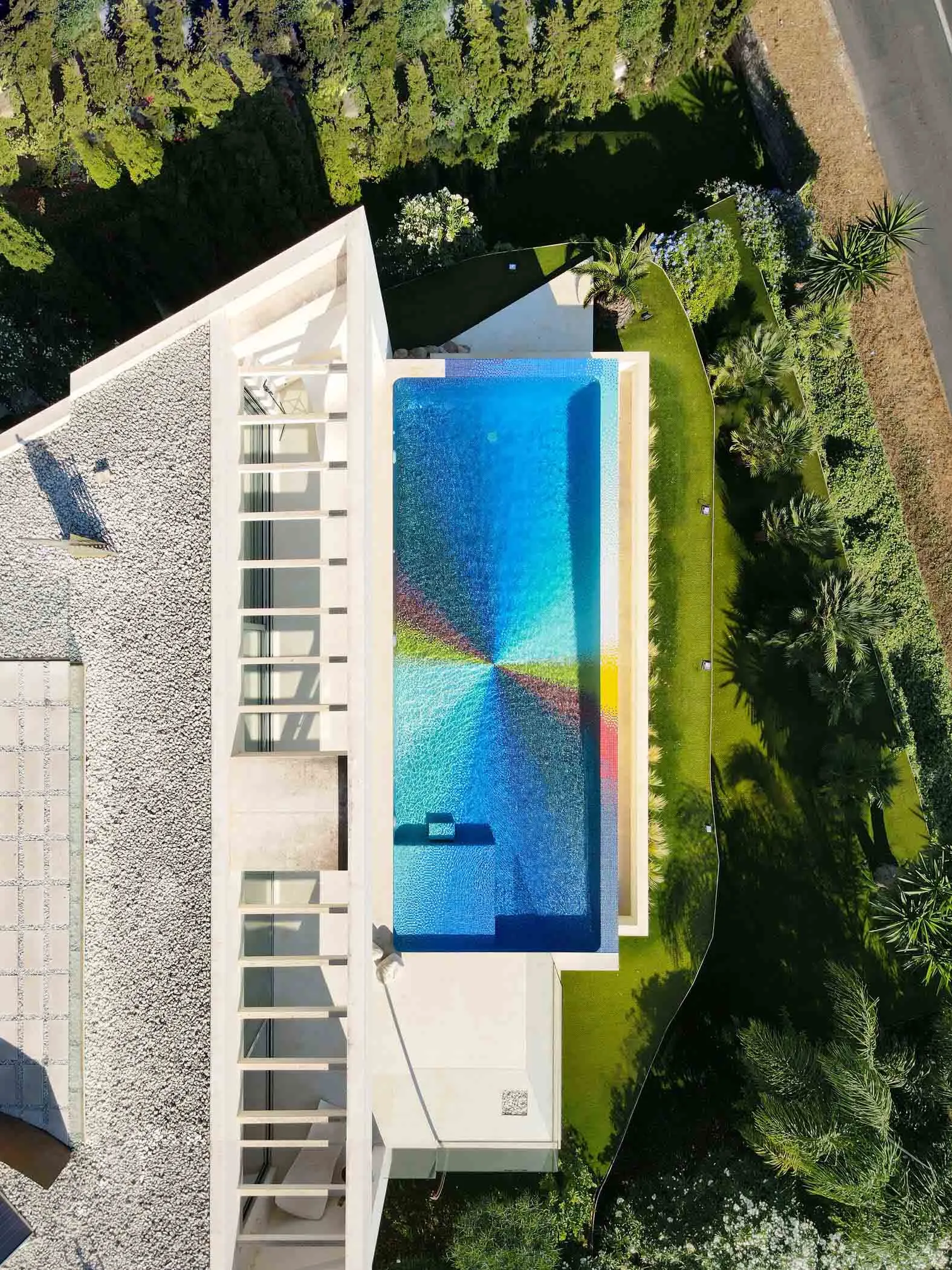 A modern outdoor swimming pool surrounded by greenery and glass.