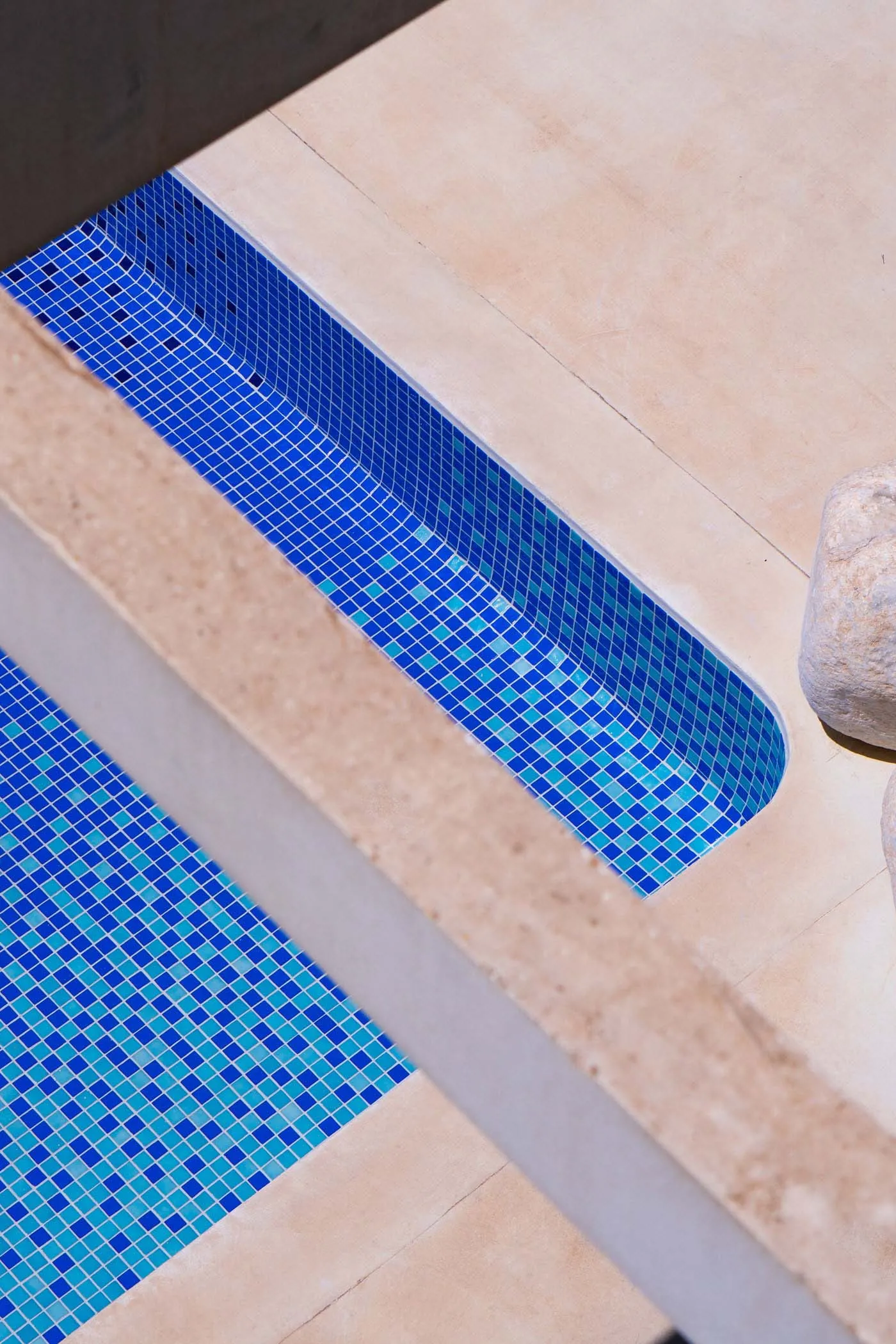Modern swimming pool exterior with blue tiled water and beige concrete deck.