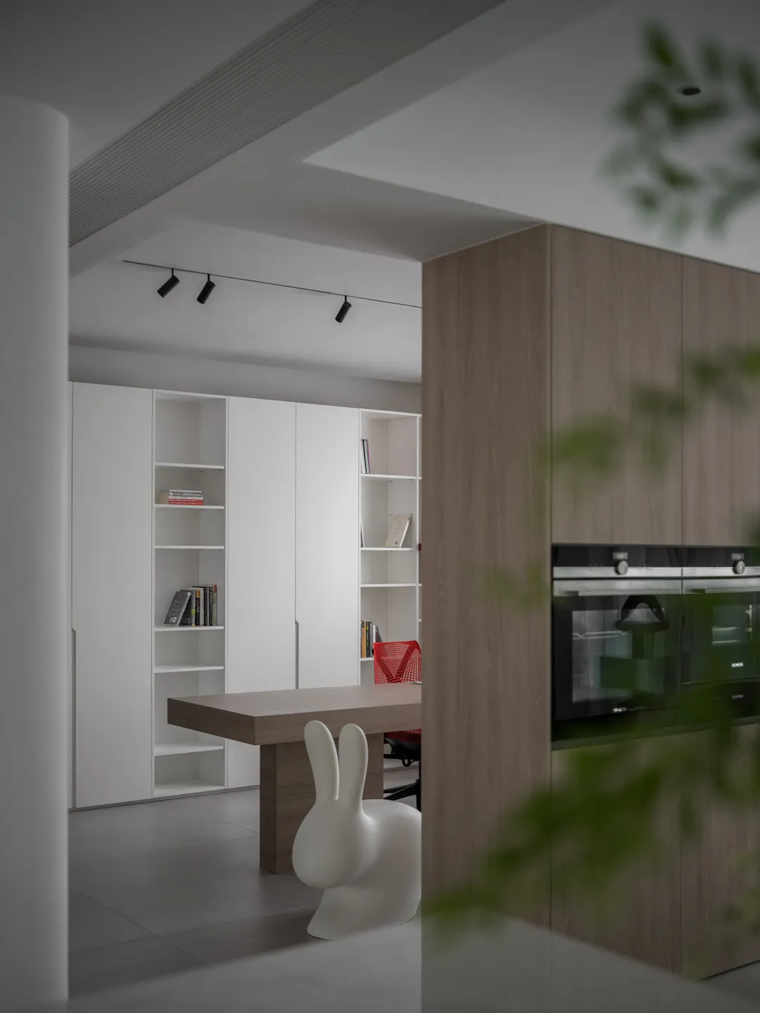 A minimalist residential kitchen with a wooden table, white chairs, and white cabinets.