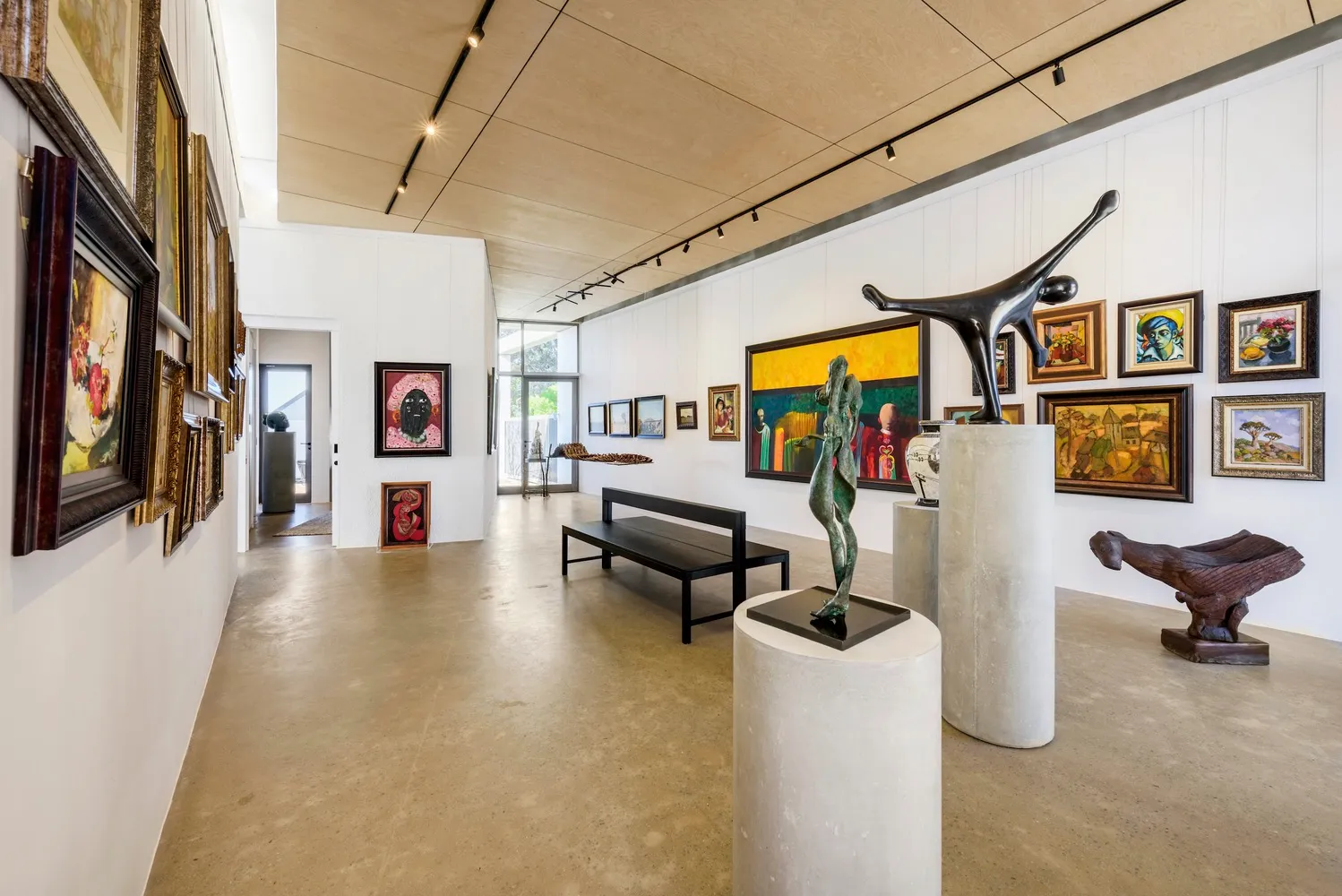 Modern art gallery with sculptures on concrete pedestals, metal figures, and paintings on the walls.