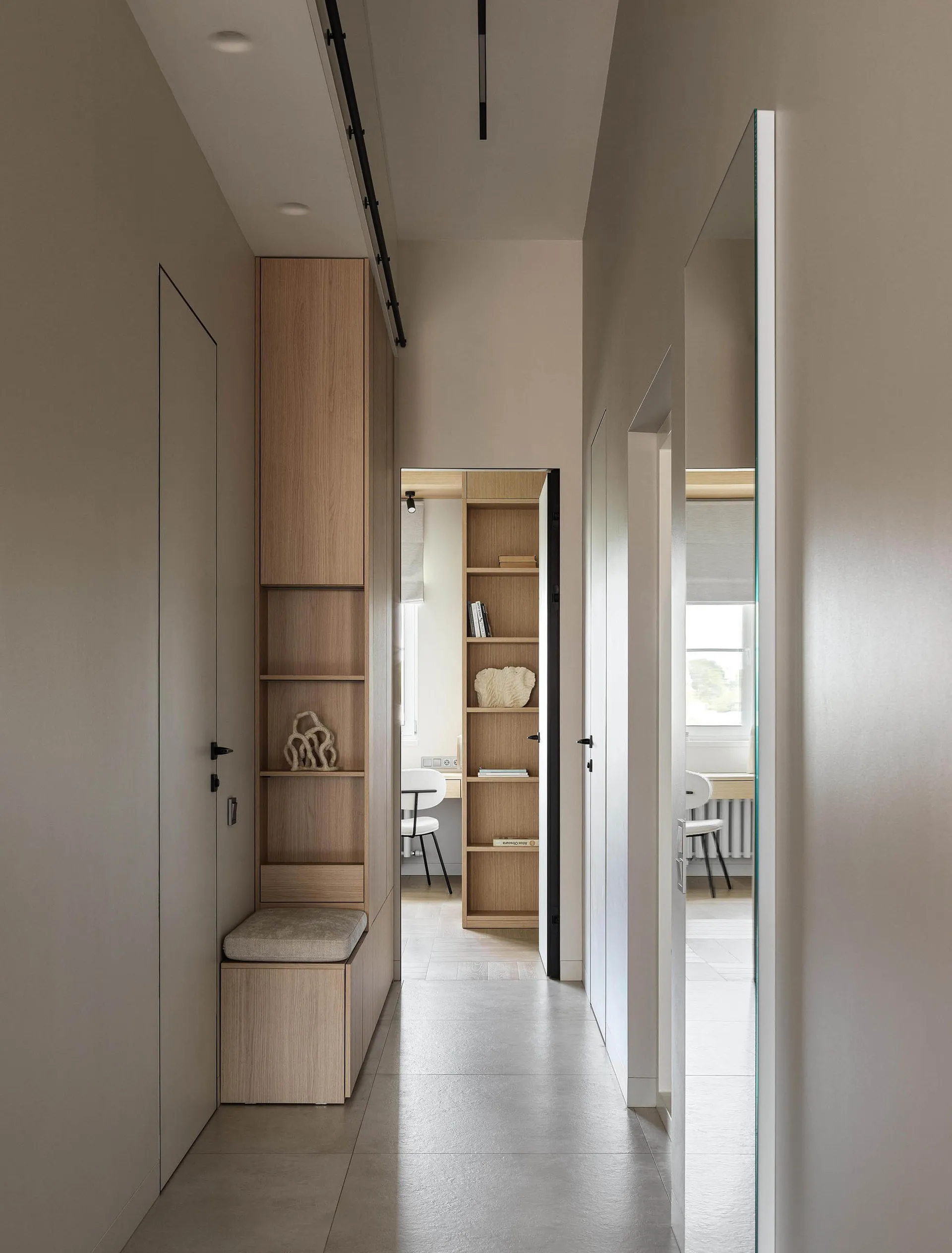 A modern interior entryway with wooden cabinets, shelves, and a long corridor.