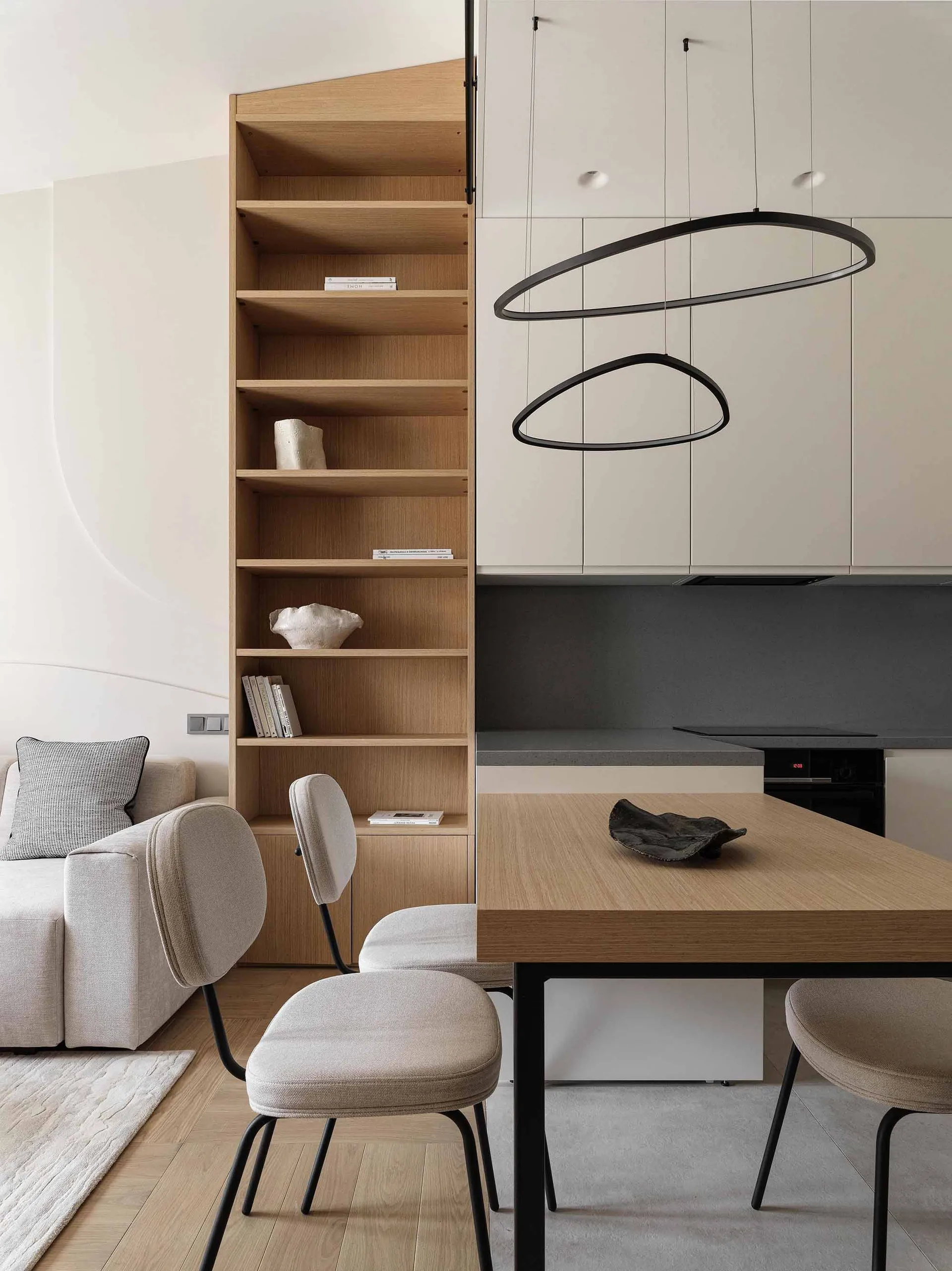 A modern minimalist kitchen featuring light-colored wooden shelves and a dining table with contemporary lighting fixtures.