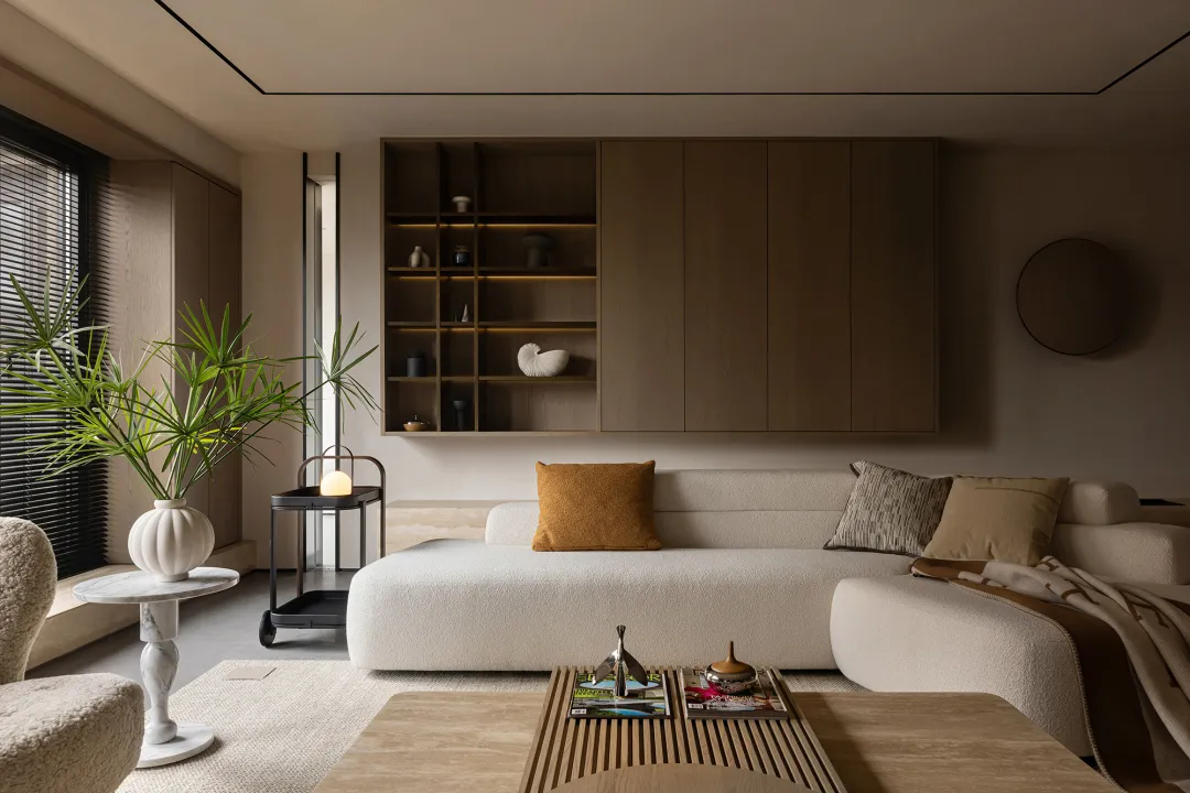 A modern living room with a minimalist design, featuring neutral-toned furniture, a large window, a coffee table with magazin