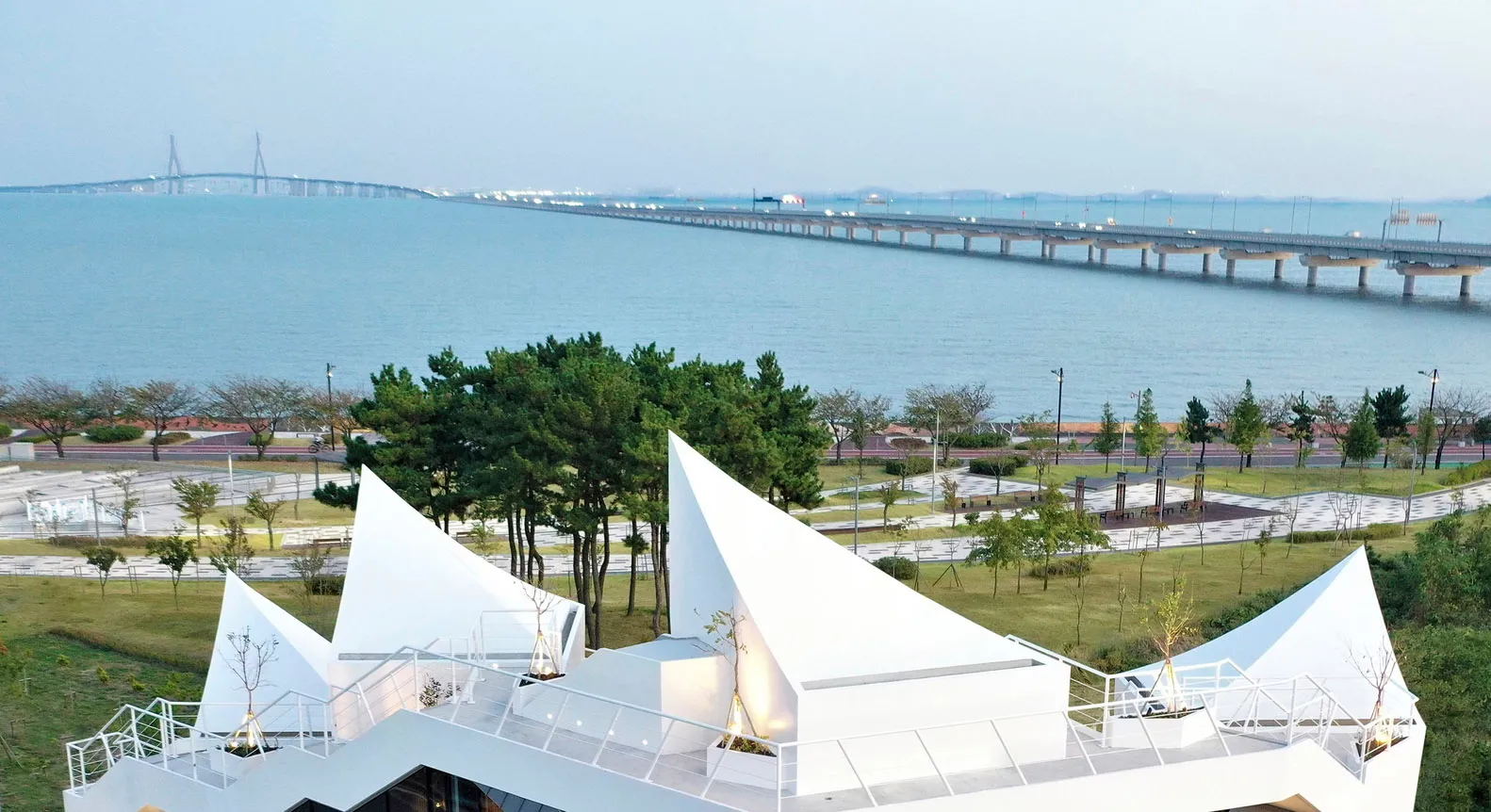 現代公園展示混凝土步道、綠意植栽,以及背景中的橋樑。